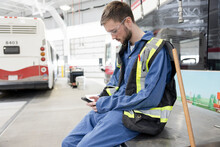 Male Worker Taking A Break With Smart Phone In Maintenance Facility
