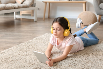 Sticker - Little girl with headphones and tablet computer listening to audiobook at home