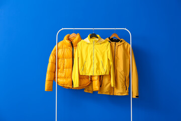 rack with bright jackets on color background