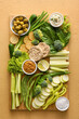 © Pixel-Shot - Wooden board with different green vegetables and bowls with sauce on color background