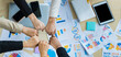 © Bangkok Click Studio - Table top view of a wooden conference table with charts and graphs papers on the table and six business women's hands put together cheering. Concept for business meeting