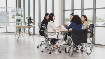 Wall Mural - Asian business women and handicap woman sitting on wheelchair are in meeting together on the table in office. Concept for business meeting