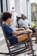 Happy Father And Son Talking In Rocking Chairs On Patio