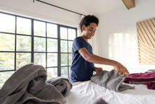 Boy Folding Laundry On Bed At Home