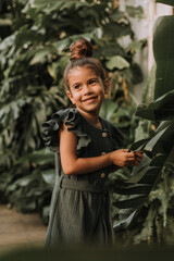 Wall Mural - The face of a little girl surrounded by tropical leaves. Closeup portrait of a beautiful swarthy baby with perfect skin and dark hair. Natural cosmetics, health, cleanliness, skin care, beauty concept