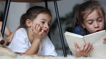 Poster - Little girls' sisters have fun reading a book lying on the floor at home.