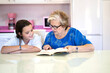 © ADDICTIVE STOCK - Elderly woman reading book with granddaughter in light kitchen at home