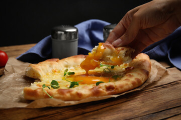 Woman eating delicious Adjarian khachapuri at wooden table, closeup