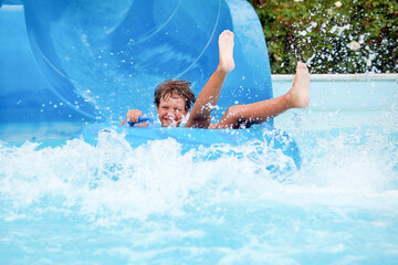 Wall Mural - happy an 8 year old boy is riding in the water Park on inflatable circles on water slides with splash