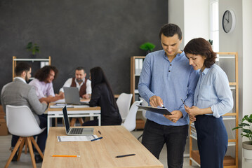 Wall Mural - Young people working with documents or report notes. Portrait of two business professionals and teammates standing near office desk with team of workers discussing new project in copy space background