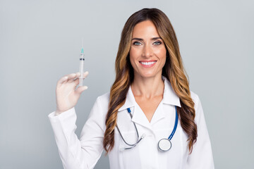 Photo of cheerful positive woman doc dressed white coat holding syringe smiling isolated grey color background