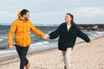 Poster - love, relationship and people concept - happy smiling couple running along autumn beach and holding hands