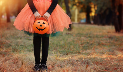 Wall Mural - Little girl in witch costume with a pumpkin bucket . Kid having fun at Halloween trick or treat. Kids trick or treating.