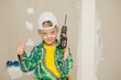 © Ermolaev Alexandr - Young boy holds a drill and shows thumbs up gesture