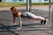 A girl standing in a pose for push up. Fitness class. The female is exercising in the park.