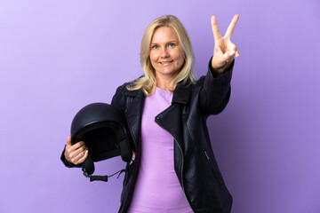 Wall Mural - Middle age woman holding a motorcycle helmet isolated on purple background smiling and showing victory sign