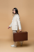 Happy Young Woman In Suit Carrying Vintage Suitcase On Beige