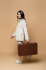 Sticker - happy young woman in suit carrying vintage suitcase on beige