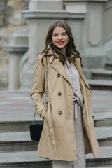 Wall Mural - Portrait of fashionable women in beige sports suit and trench coat posing on the street