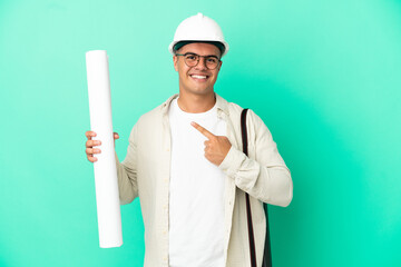 Poster - Young architect man holding blueprints over isolated background pointing to the side to present a product