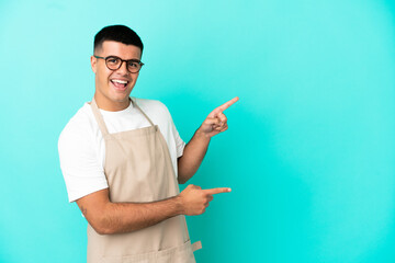 Poster - Restaurant waiter man over isolated blue background pointing finger to the side and presenting a product