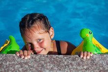 A Charming Little Girl Holds On To The Edge Of The Pool And Smiles Sweetly. 