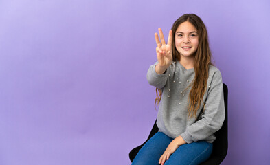 Little caucasian girl sitting on a chair isolated on purple background happy and counting three with fingers