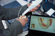 Denture scanning process. Checking teeth with an intraoral scanner. Dental intraoral scanner in hands in a suit. Monitor with video display from device in background. Electronic dental  scanner