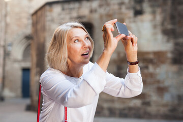  Mature woman is taking photos on her camera while journey through the city. High quality photo