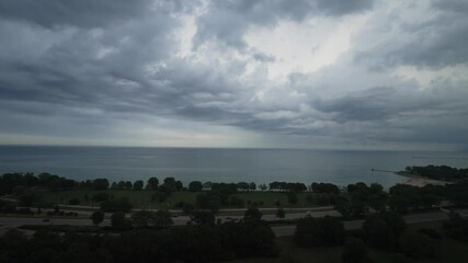Wall Mural - Aerial panning view of dramatic undulating storm clouds part of a weather front rolling across the sky over the water of Lake Michigan and Lake Shore Drive with rain and thunderstorms in the distance.