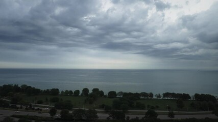 Wall Mural - Aerial panning view of dramatic undulating storm clouds part of a weather front rolling across the sky over the water of Lake Michigan and Lake Shore Drive with rain and thunderstorms in the distance.