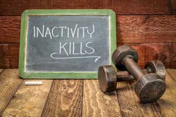 Wall Mural - inactivity kills motivational concept, white chalk writing on a slate blackboard with a pair of vintage dumbbells, sedentary lifestyle, fitness and personal development