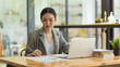 © bongkarn - Focused Asian female office worker sitting at the desk, working on project