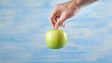 Male Hand Holding Green Apple On The Blue Background.