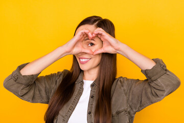 Poster - photo of pretty happy young woman make fingers heart shape look eye smile isolated on yellow color b