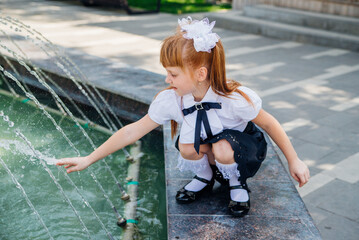 A little girl, an elementary school student, is playing merrily near the fountain .The child will refresh himself on a hot day.