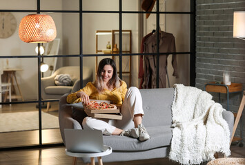 Beautiful young woman eating tasty pizza at home in evening