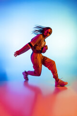 Young sportive girl dancing hip-hop in stylish clothes on colorful background at dance hall in neon light. Youth culture, movement, style and fashion, action.