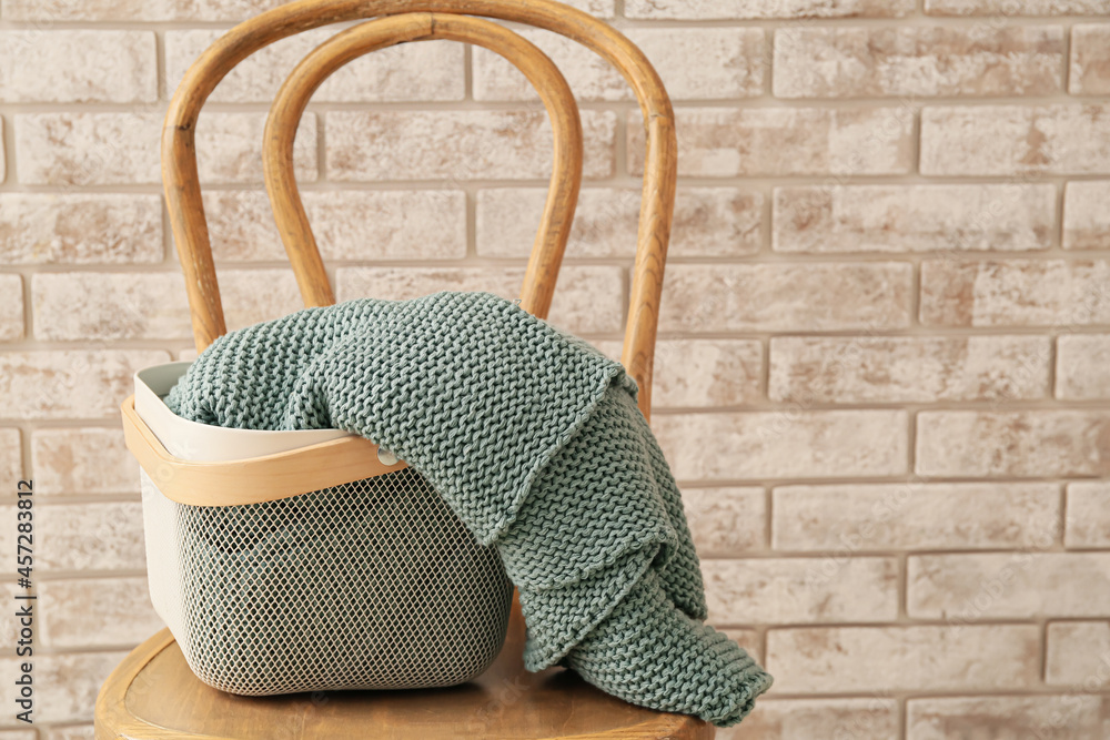 Basket with knitted plaid on chair near brick wall