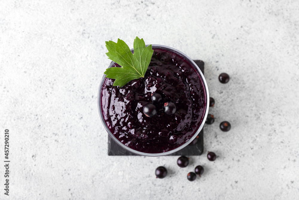 Bowl with delicious black currant jam on light background