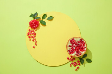 Empty podium for cosmetics with ingredients of red pomegranate extract and pomegranate seeds, flakes and leaves on light green background