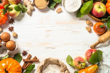 Autumn baking background. Flour, sugar, apples, pumpkin and spices at white kitchen table. Top view image with copy space.