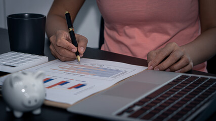 Hands of money making and calculating on desk about home office expenses. An accountant uses a calculator and computer holding a pen pointing to a graph document.