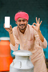 Indian milkman showing smartphone screen at dairy farm.