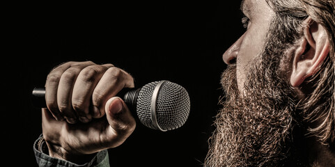 Wall Mural - Bearded man in karaoke sings a song into a microphone. Male attends karaoke. Male singing with a microphones. Man with a beard holding a microphone and singing