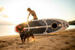 © Cavan - Happy dog with his tongue out and woman with a paddleboard behind him