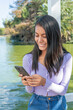 © Cavan - Portrait of a Young Woman Responding to a Text Message While Smiling. The young Latina is in a public park.