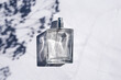 Transparent bottle of perfume with spray on white marble surface. Clear glass without lid. Trending concept in natural materials with plant shadow. Luxury presentation.