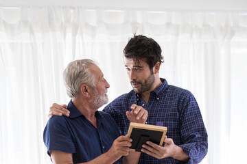 Wall Mural - Senior Father and Adult Son talking and looking a frame picture at home