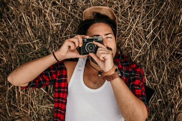 Poster - Serbian male photographer lying on a straw and taking pictures of rural landscape on vintage camera